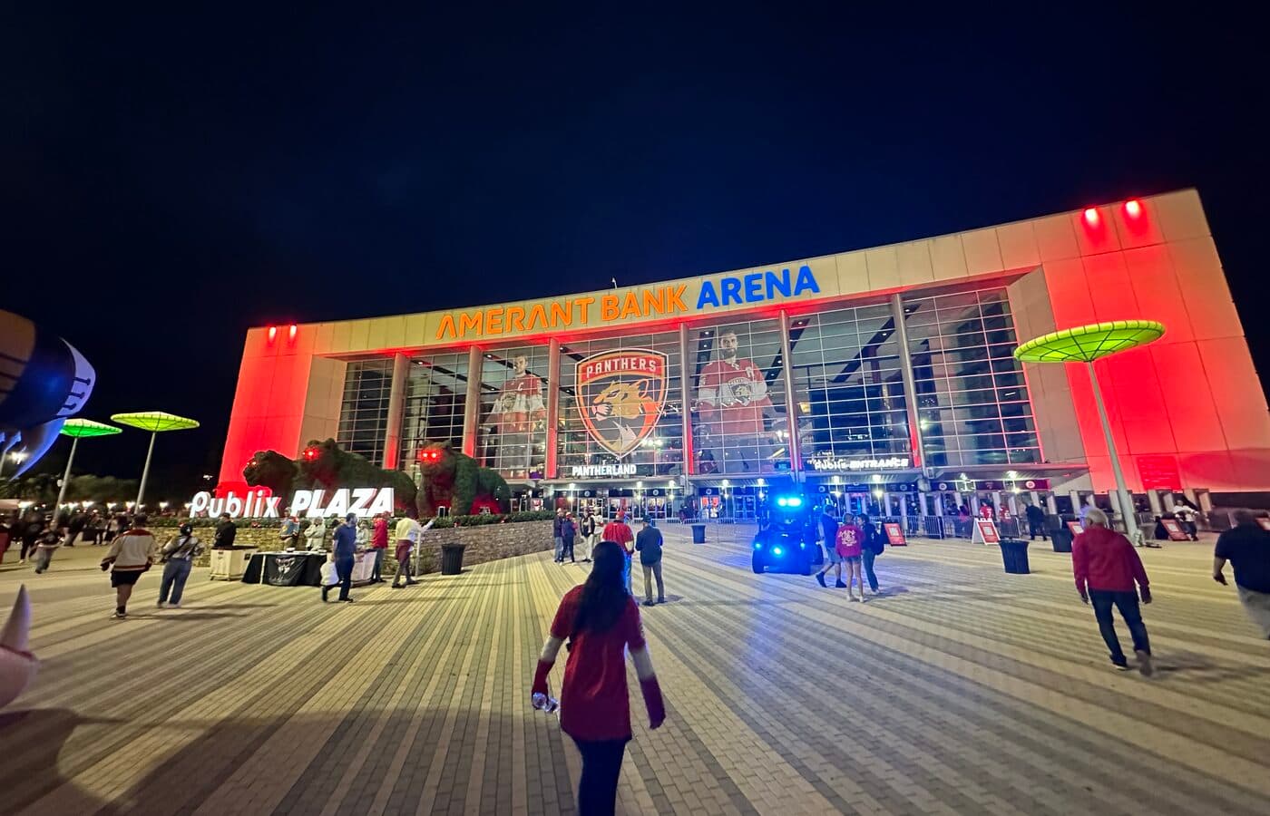 Amerant Bank Arena’s main entrance lit red at night, with its sign, the Florida Panthers logo and the Publix Plaza forecourt in front