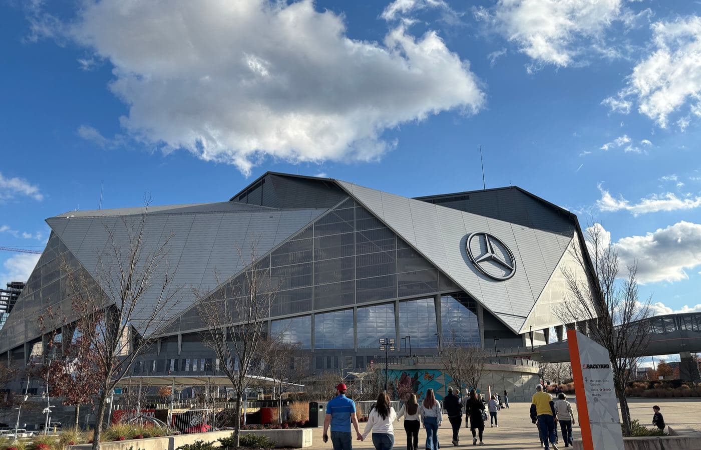 Mercedes-Benz Stadium’s angular silver exterior and glass front, with fans walking on the plaza outside