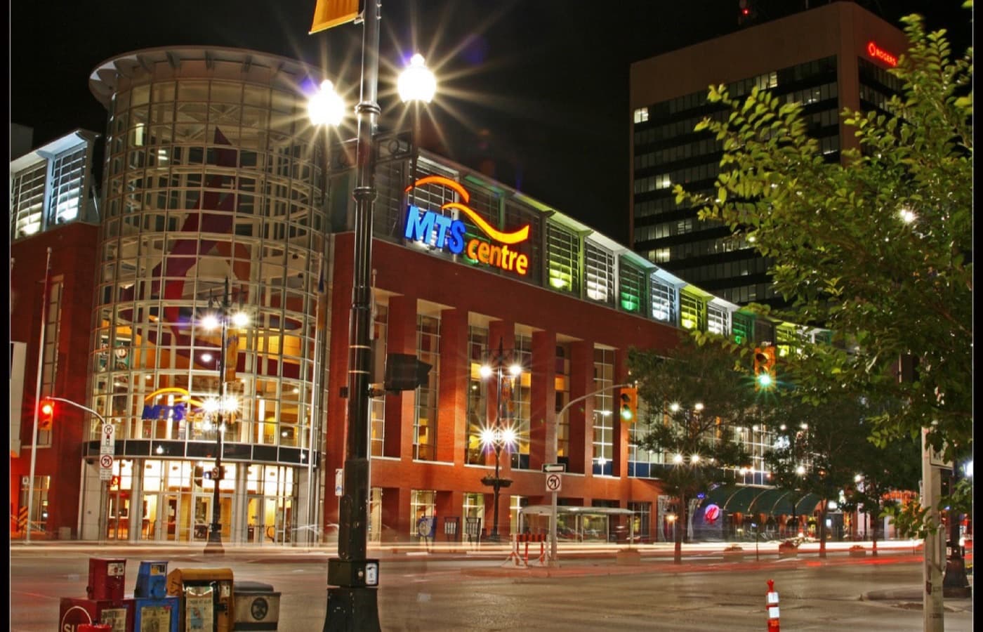 The glass rotunda and brick front of the downtown Winnipeg arena that is home to the Winnipeg Jets, lit up at night. The photo predates the building’s current name and shows its former MTS Centre signage.
