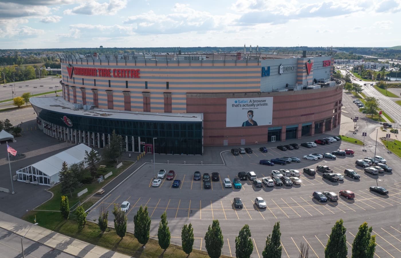 An aerial view of Canadian Tire Centre’s curved exterior, with its lit sign and Ottawa Senators logo above the parking lot in Kanata