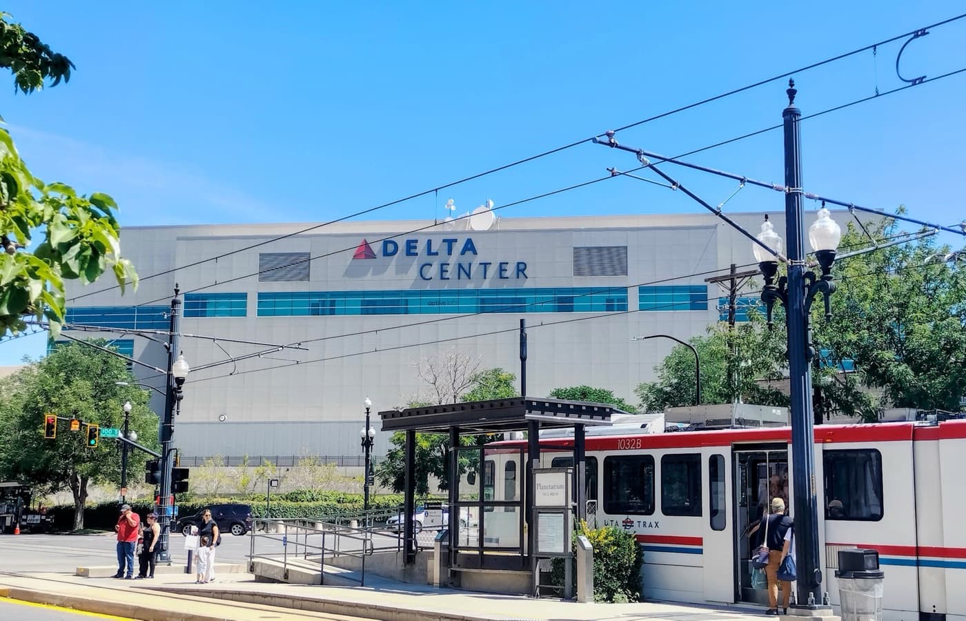 Delta Center’s grey facade and blue entrance windows in downtown Salt Lake City, with a UTA TRAX train stopped in front
