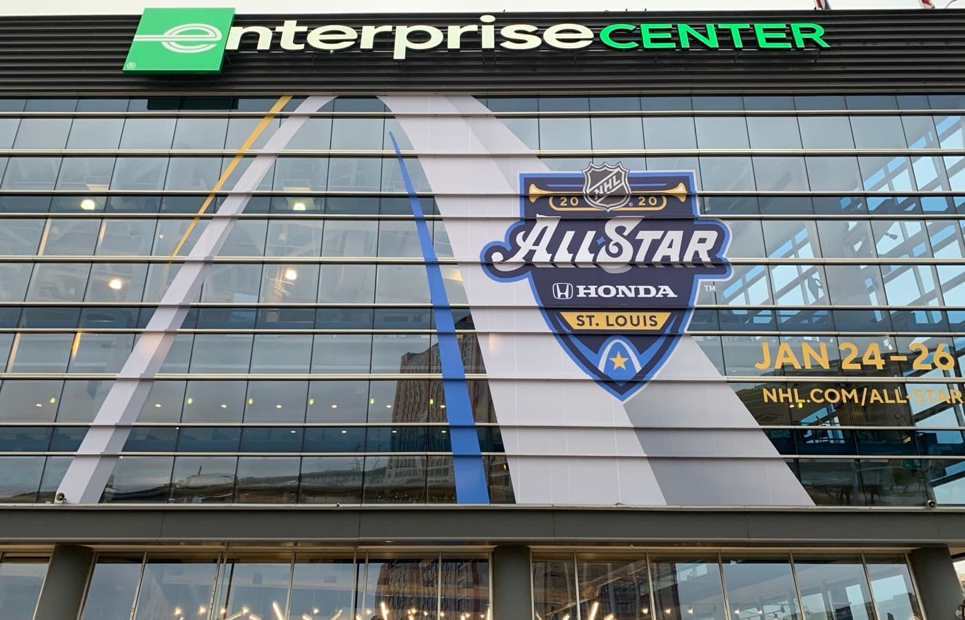 The Enterprise Center sign and glass exterior in downtown St. Louis, with a Gateway Arch mural and 2020 NHL All-Star Game signage on the facade