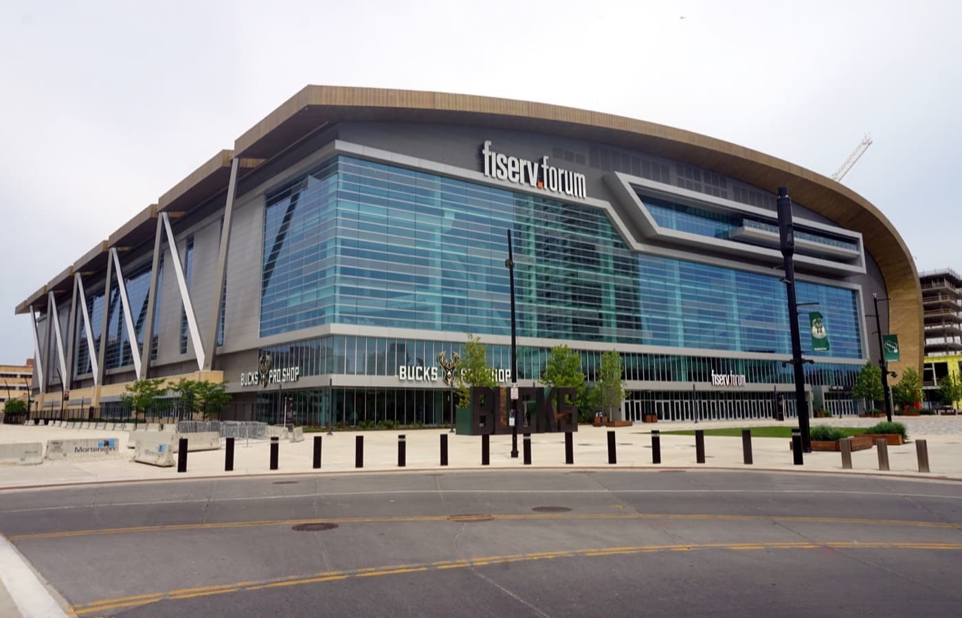 Exterior of Fiserv Forum in Milwaukee, with its glass facade, wood-clad canopy and the Bucks Pro Shop entrance on the Deer District plaza