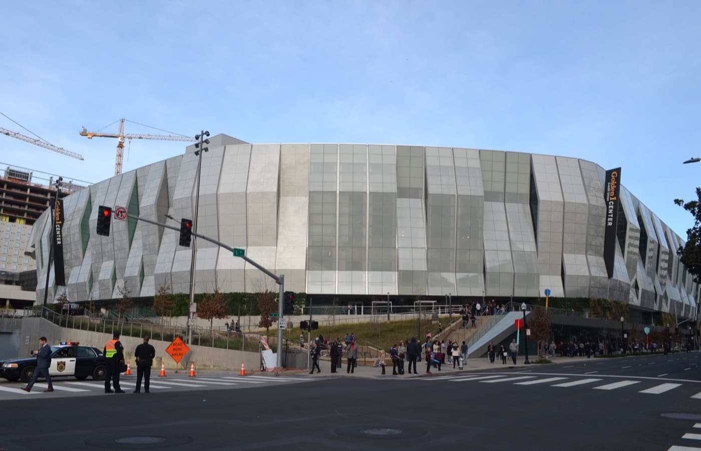 Street-level view of Golden 1 Center’s angular glass and metal exterior in downtown Sacramento, with pedestrians near the entrance plaza