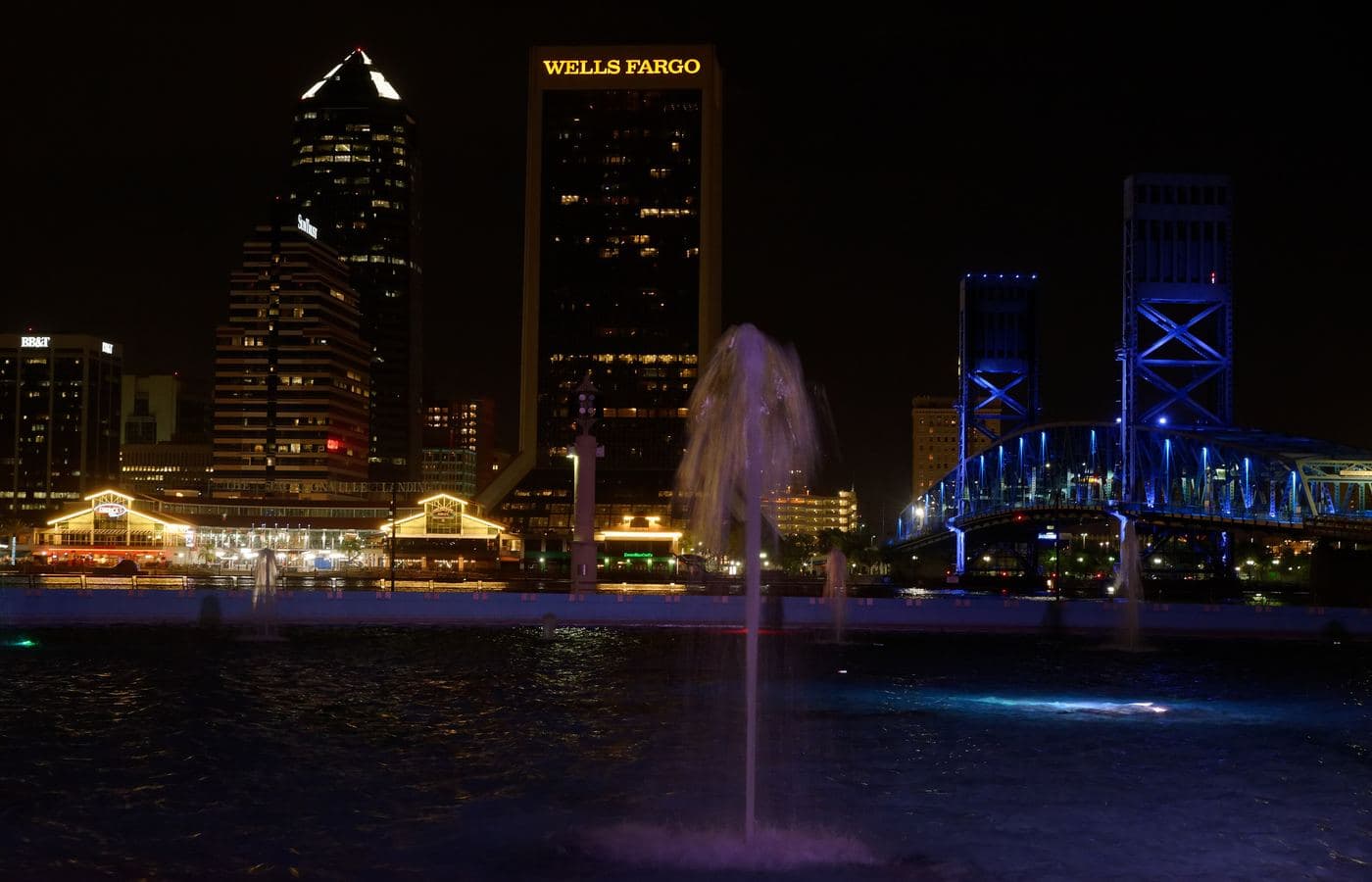 Downtown Jacksonville’s towers and the Main Street Bridge lit blue at night, seen across the St. Johns River from Friendship Fountain