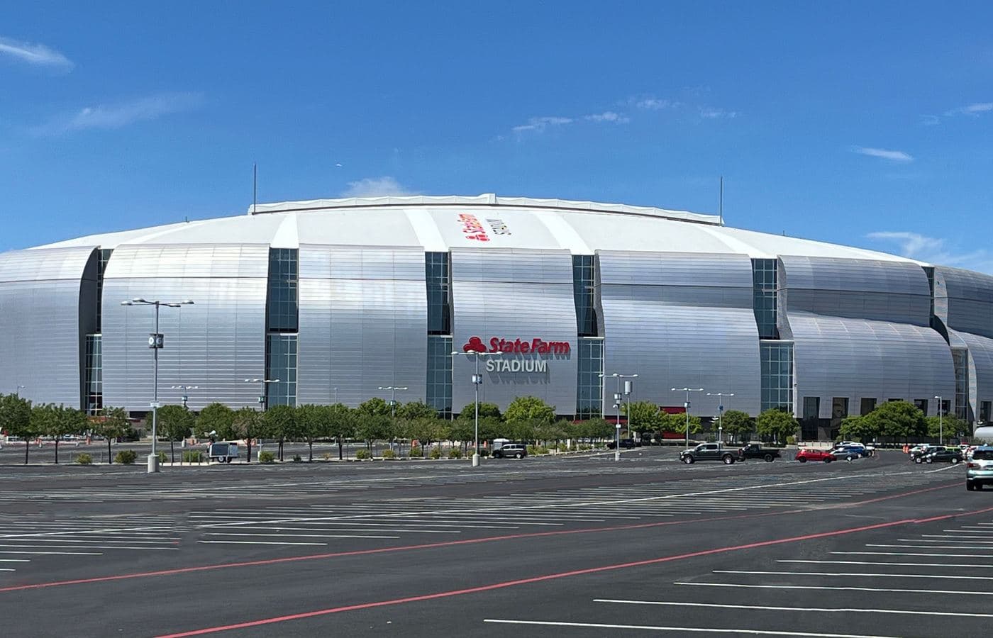 State Farm Stadium’s silver exterior in Glendale, Arizona, seen across a parking lot