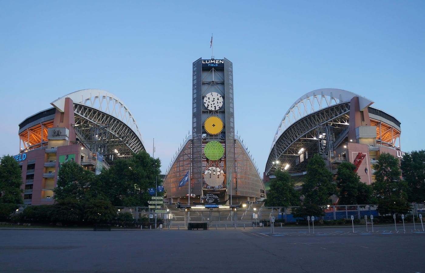 The north side of Lumen Field at dusk, its tower sign between the two arched roof trusses above an empty plaza