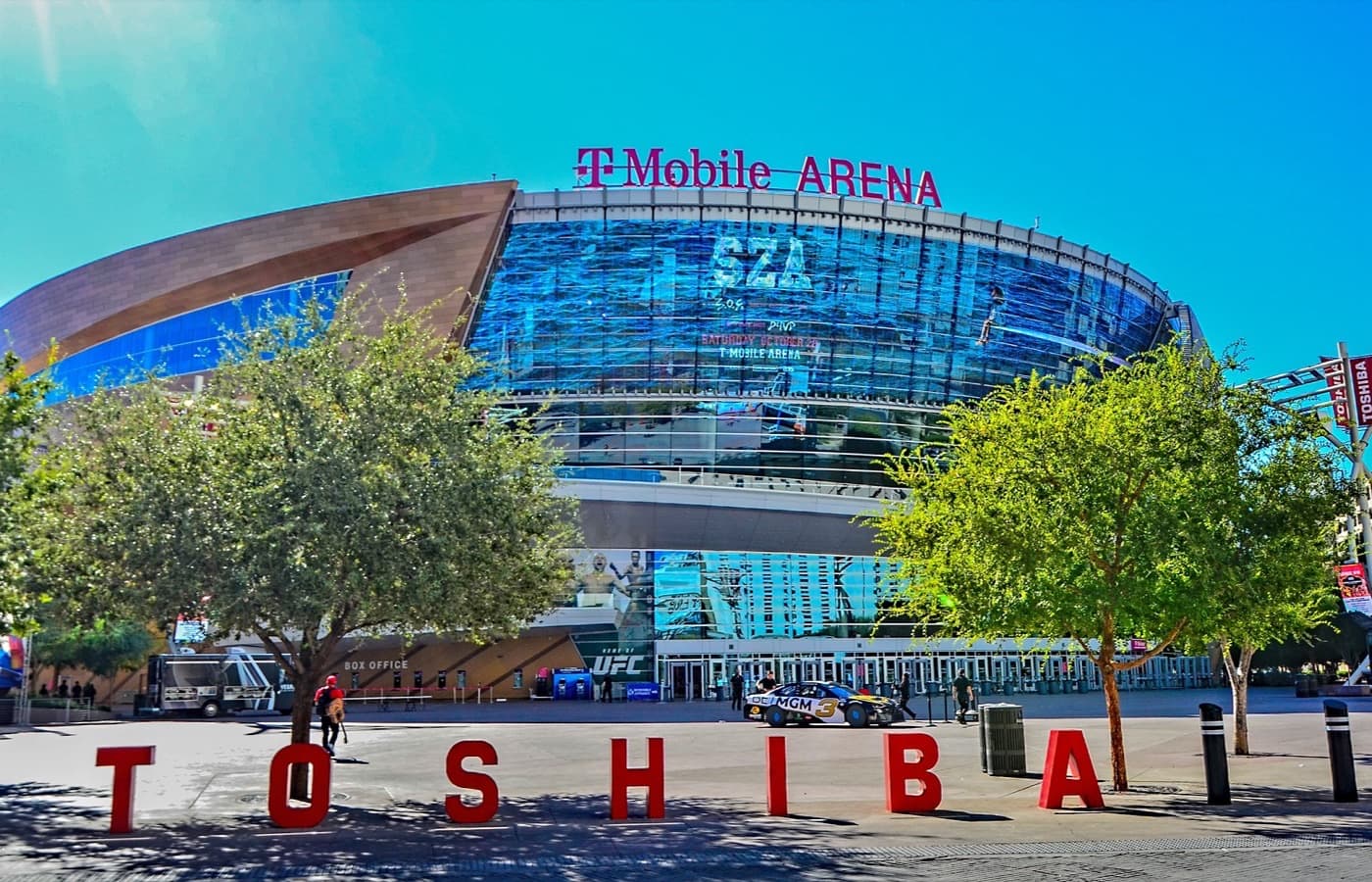 T-Mobile Arena’s curved glass-and-steel facade rising behind the red Toshiba Plaza letters, with the T-Mobile Arena sign on the roofline