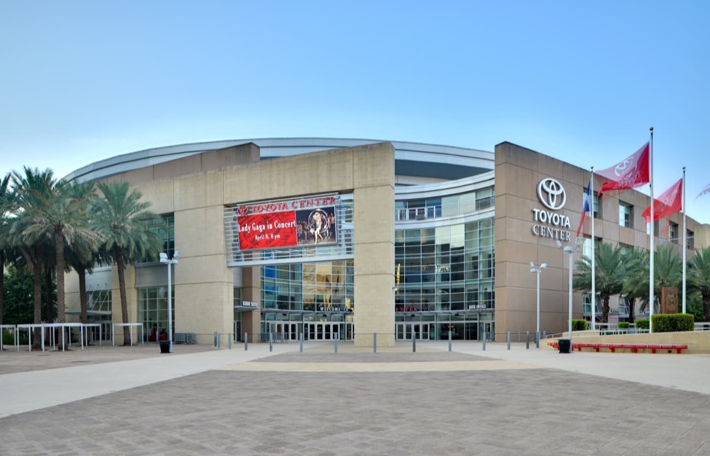 The Toyota Center entrance in downtown Houston, with palm trees, flags and an event marquee above the glass doors